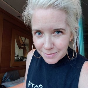 Brooke Gallagher, a blonde, white woman with blue eyes wears a sleeveless black top and large hoop earrings and slightly smiling into the camera