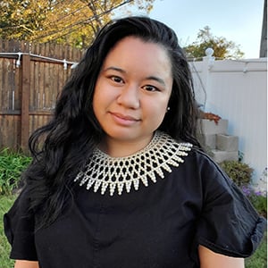 A headshot of Jessica in an outdoor setting, wearing an elaborate pearl collar necklace.