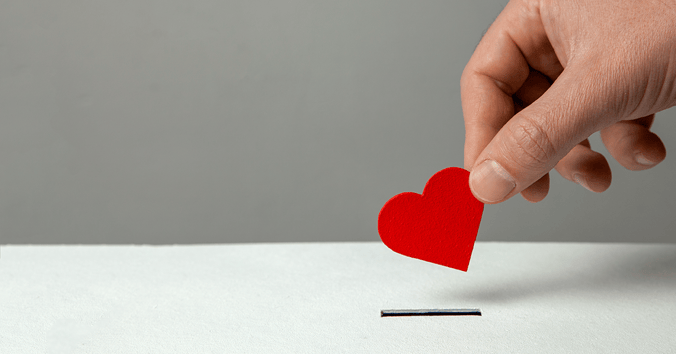 A hand posting a small red heart into a donations box