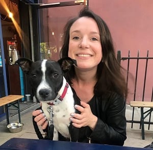 Raphaelle Roux, a woman in her thirties with brown hair, sitting at an outside pub table with a black and white staffy on her lap.