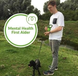 James is stood outside on a field, trying to keep his small dog under control on her lead. He is wearing a white t-shirt so it must have been warm when the photo was taken!