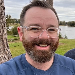 A headshot of Ben Park, a white man with dark hair and a beard, smiling into the camera