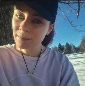 A headshot of Jordan Kennedy enjoying a sunny winter day at the park in a cap and pink jumper.