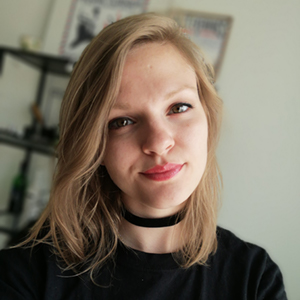 A headshot of Katarina, a woman with blonde hair, wearing a black t-shirt and smiling into the camera.