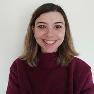 A headshot of Nina Primeraki, wearing a purple fluffy jumper, and smiling into the camera.