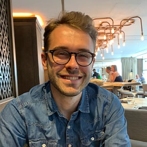 A headshot of Robin Sheffield, a man with brown hair wearing a denim shirt and glasses, smiling into the camera.