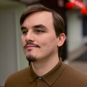 A headshot of Tom a man with dark brown hair looking off camera