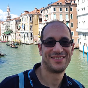 Alessandro Signoretti, wearing sunglasses, stands on a bridge in Venice
