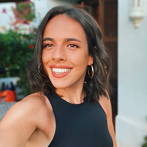 Amy Wilkes, with long dark hair, wearing a black sleeveless top, smiles into the camera