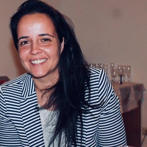 Aura Silva, a woman with long dark brown hair wearing a striped blazer