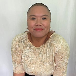 Clarissa Arocena, a person wearing a yellow shirt, sitting in a chair, and smiling brightly at the camera.