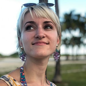 Lauren DeLucia, a woman with light blonde hair, wearing a patterned summer dress, with the palm trees of Miami Beach behind her.