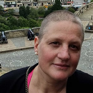 Liv Nilssen, a white woman in her 40s with very short brown and silver hair. In the background a view from Edinburgh Castle showing other visitors, gardens, the street and shops.
