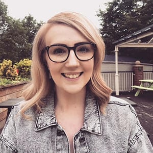 Sarah Stopford, a woman with wavy blond hair and glasses, smiles into the camera