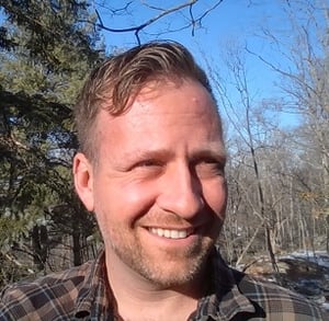 Scotty Arnold, a man in his thirties with blond hair, smiles outdoors.