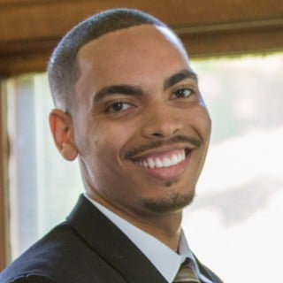 Zack Moore, a Black man, wearing a suit and tie and smiling into the camera