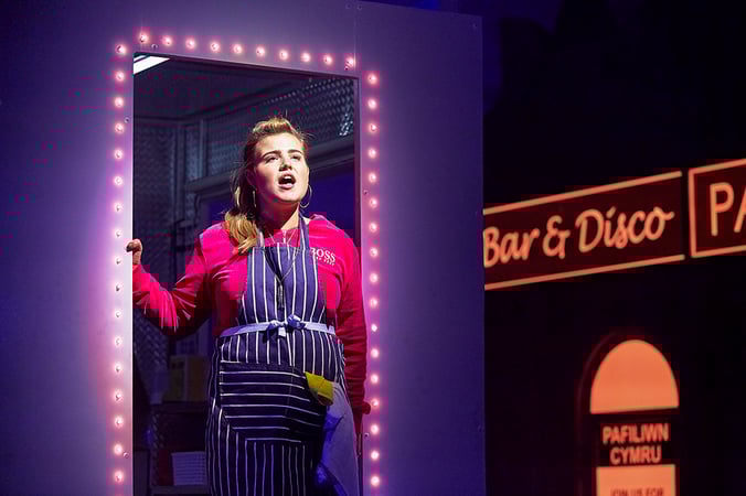 An actor stands in a doorway of a stage set that resembles an American diner