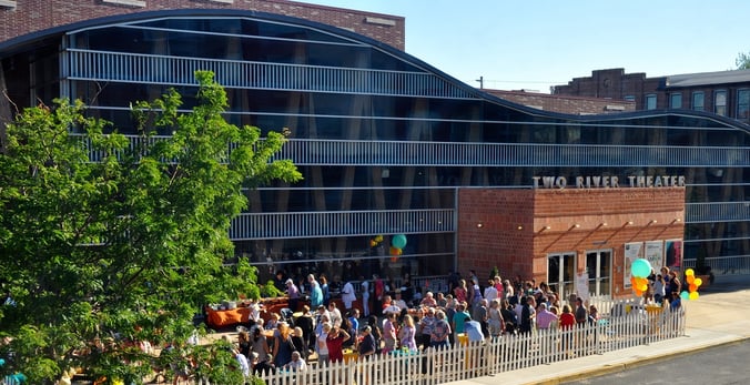 Exterior of Two River Theater, where a large crowd is gathered in the sunshine