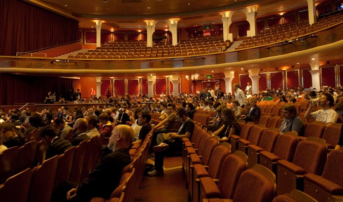 A traditional theatre with rows of seats half filled by audience members