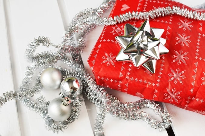 A festive gift, wrapped in bright red paper with silver tinsel, bows and baubles.